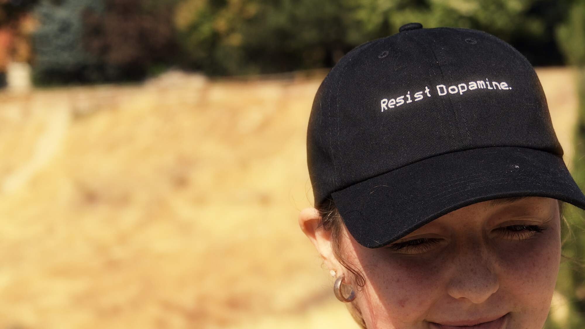 The black hat pulled low over a woman's eyes, Resist Dopamine stitched across the front